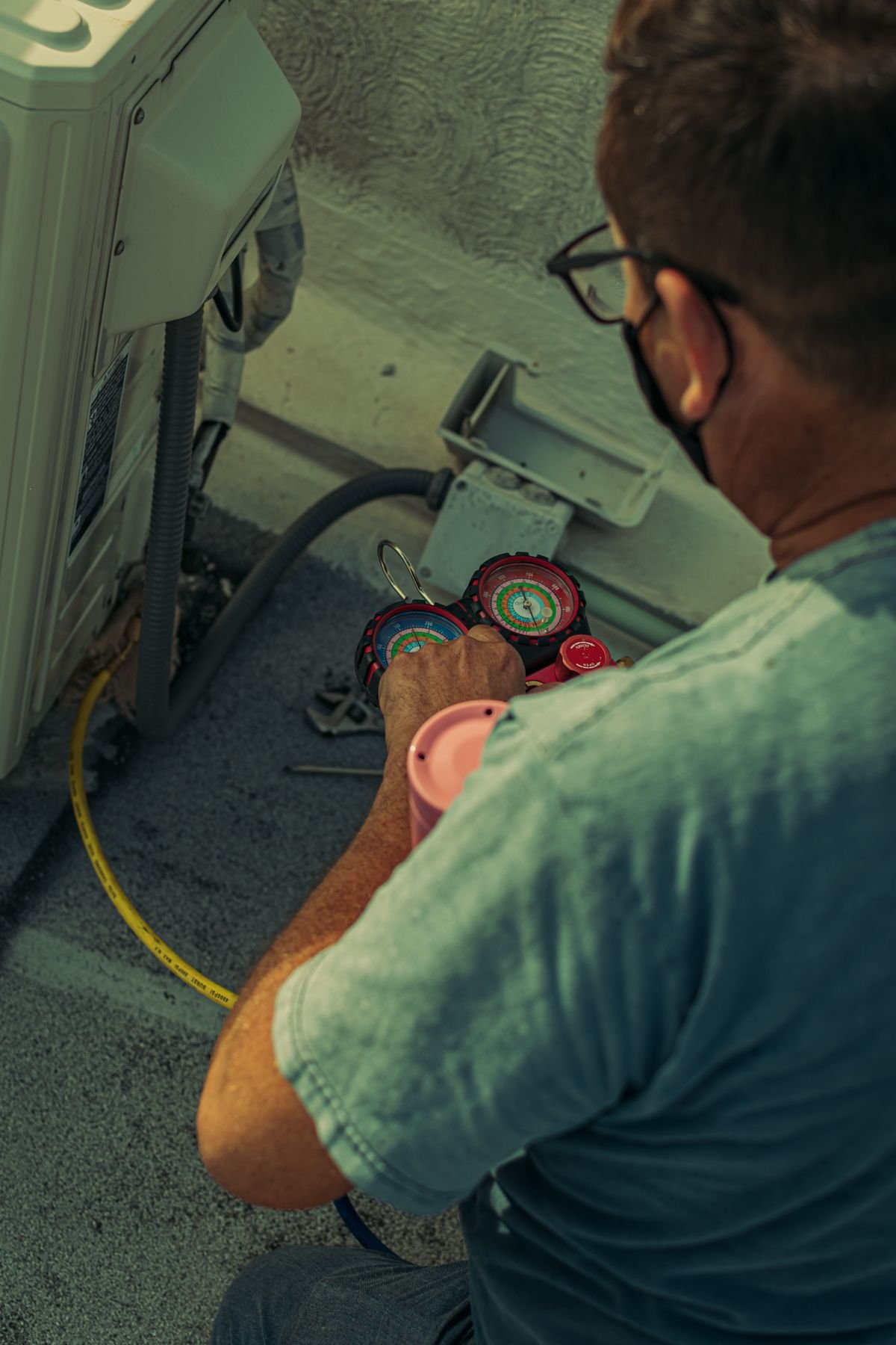 HVAC technician servicing an outdoor air conditioning unit with gauges